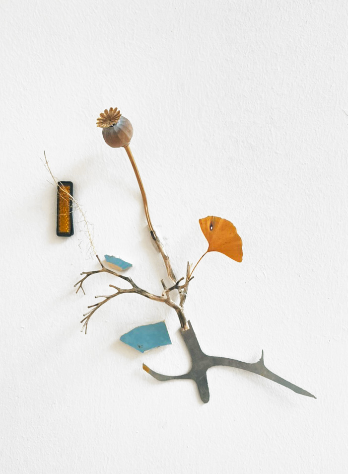 An assemblage of branches, dried flowers and found objects on a white wall