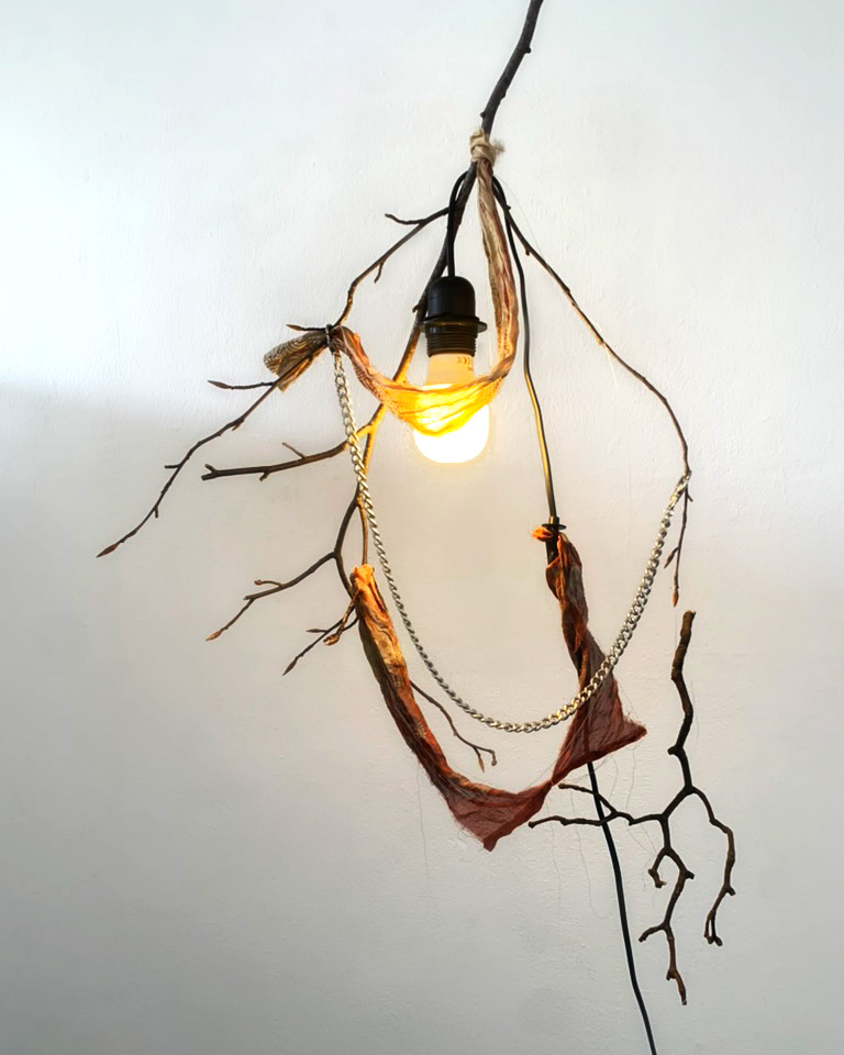 A sculptural light made with branches, fabric and chain